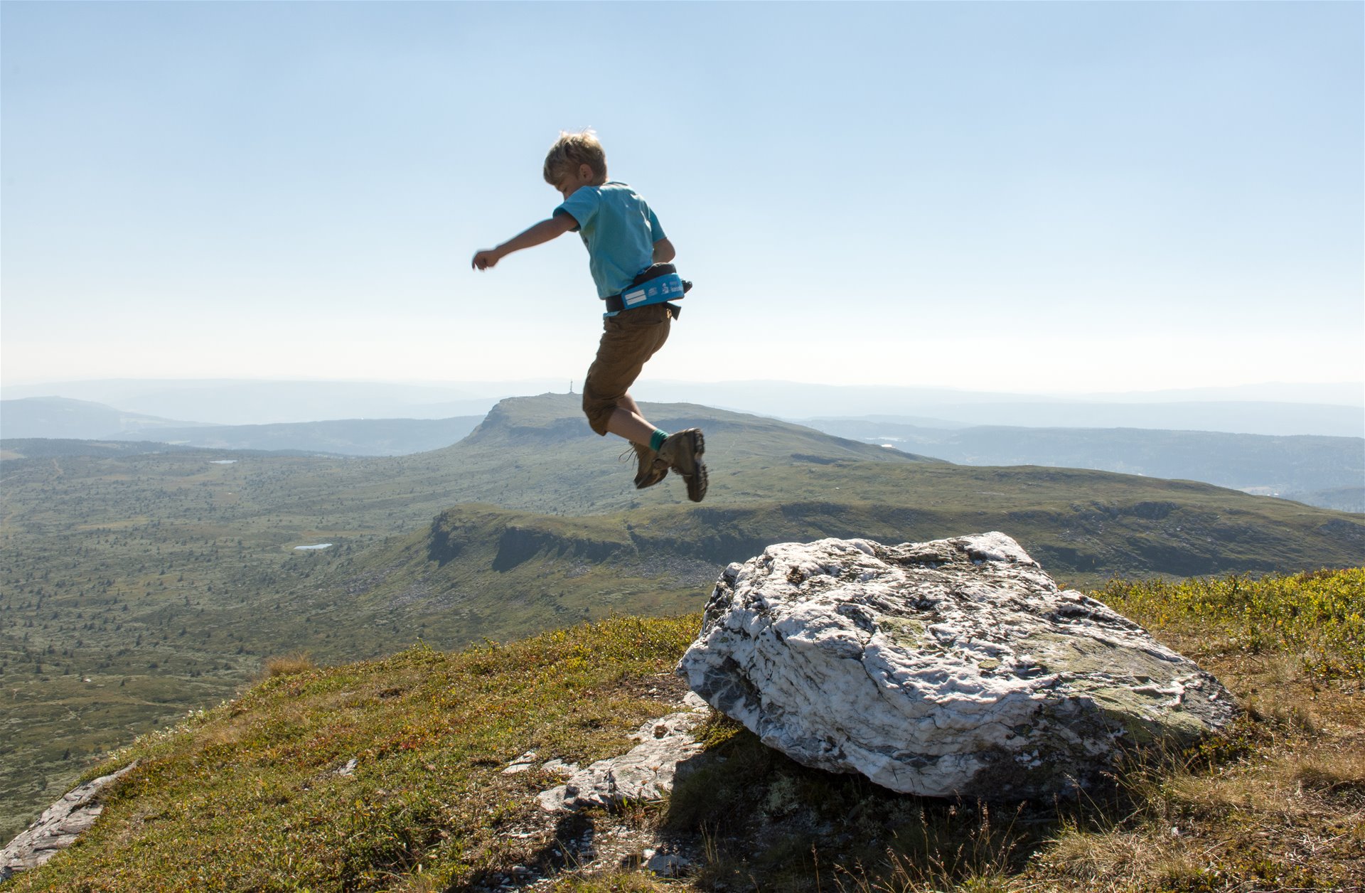 Boy jumping from rock on mountain.